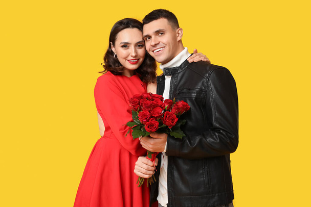 Любящая молодая пара с букетом красивых цветов на желтом фоне. Празднование Дня Святого Валентина - Фото, изображение