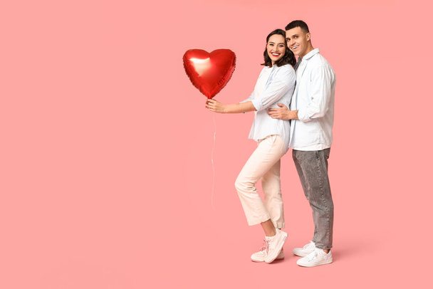 Αγαπημένο νεαρό ζευγάρι με μπαλόνι σε σχήμα καρδιάς σε ροζ φόντο. Εορτασμός της ημέρας του Αγίου Βαλεντίνου - Φωτογραφία, εικόνα