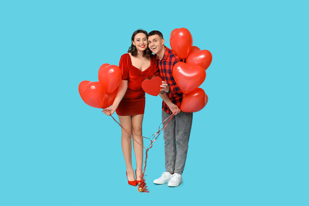 Amante pareja joven con globos en forma de corazón y caja de regalo sobre fondo azul. Celebración del Día de San Valentín - Foto, imagen