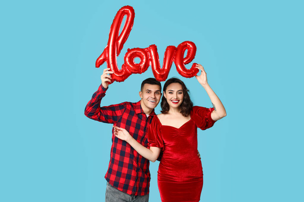 Любящая молодая пара с воздушным шариком в виде слова LOVE на синем фоне. Празднование Дня Святого Валентина - Фото, изображение