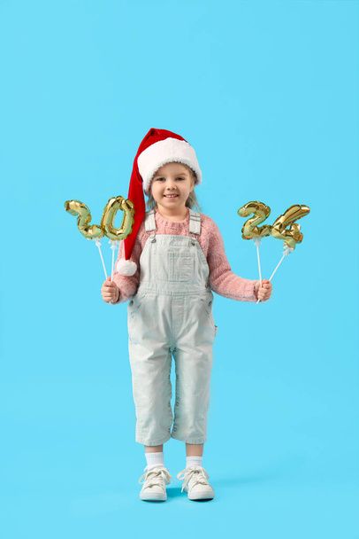 Cute little girl w Santa kapelusz z rysunkiem 2024 na niebieskim tle - Zdjęcie, obraz