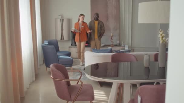 Foto completa de la vendedora en la tienda de muebles dando escaparate de los modelos disponibles de sofá para el cliente masculino - Metraje, vídeo