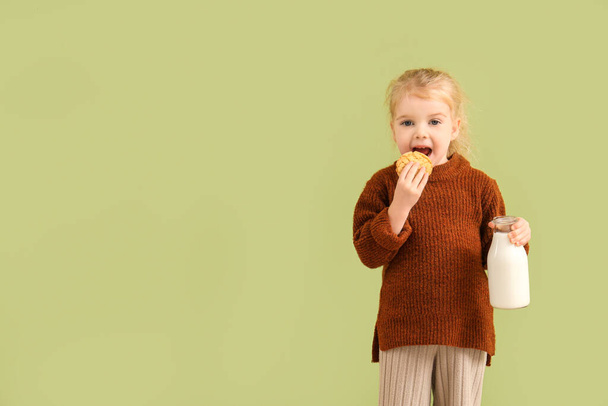 Yeşil arka planda bir şişe sütle kurabiye yiyen tatlı küçük kız. - Fotoğraf, Görsel