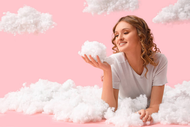 Young woman with white clouds lying on pink background - Фото, изображение