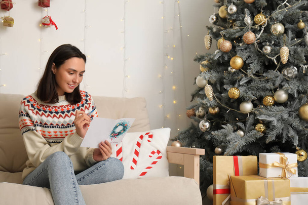Csinos fiatal nő ír üdvözlőlapot karácsonyi ünnepségre otthon - Fotó, kép