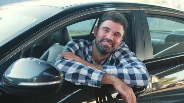 Hymyilevä nuori mies istuu autossa katsellen kaupungin avointa ikkunaa. Liikenne, elämäntapa, ihmisten käsite. Hidastus - Materiaali, video