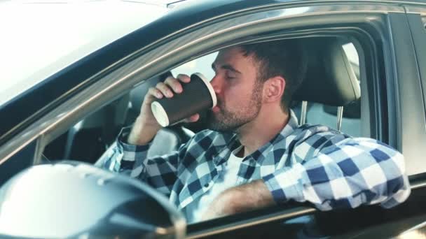Nuori mies istuu autossa juoden kahvia. Liikenne, elämäntapa, ihmisten käsite. Hidastus - Materiaali, video