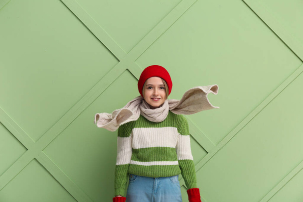 Χαριτωμένο μικρό χαρούμενο αγόρι με χειμωνιάτικα ρούχα σε πράσινο φόντο - Φωτογραφία, εικόνα