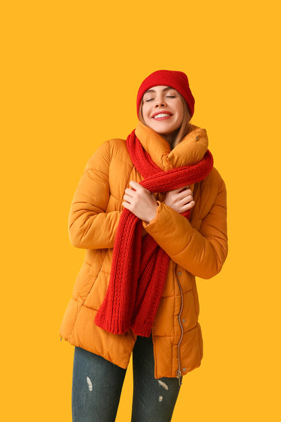 Красивая молодая счастливая женщина в теплой зимней одежде на желтом фоне - Фото, изображение