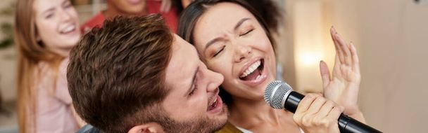 Gemeinsam singen. Junge aufgeregte Paare oder Freunde halten Mikrofone in der Hand und singen zusammen, während sie mit Freunden Karaoke spielen. Gruppe hat Spaß bei Karaoke-Heimparty - Foto, Bild