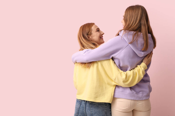 Bella giovane donna che abbraccia sua madre su sfondo rosa. Giornata internazionale dell'abbraccio - Foto, immagini