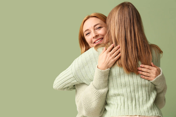 Νεαρή γυναίκα αγκαλιάζει τη μητέρα της σε πράσινο φόντο. Διεθνής Ημέρα Αγκαλιάς - Φωτογραφία, εικόνα