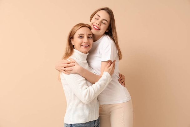 Bella giovane donna che abbraccia sua madre su sfondo beige. Giornata internazionale dell'abbraccio - Foto, immagini