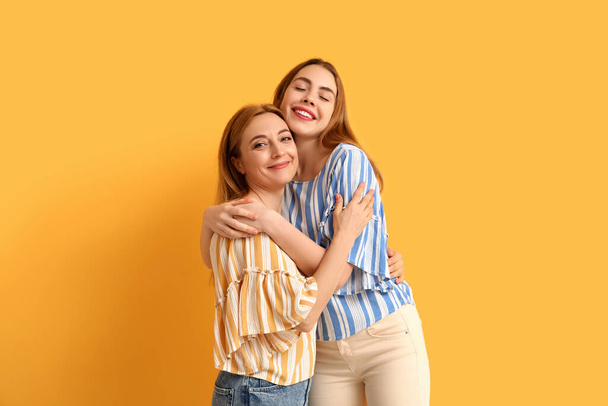 Gelukkige jonge vrouw knuffelt haar moeder op gele achtergrond. Internationale knuffeldag - Foto, afbeelding