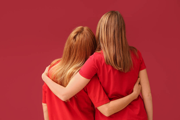 Jovem mulher abraçando sua mãe em fundo vermelho. Dia Internacional do Abraço - Foto, Imagem