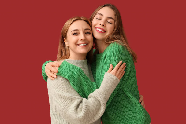 Mujer joven y feliz abrazando a su madre sobre fondo rojo. Día Internacional del Abrazo - Foto, Imagen