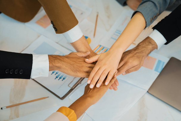 Top view of corporate diverse businesspeople putting hands together on meeting table with document scatter around at business meeting room. Represented unity, cooperation, collaboration. Ornamented. - Photo, Image