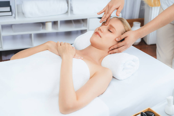 Biała kobieta ciesząca się relaksującym antystresowym masażem głowy i rozpieszczającym wypoczynkiem rekreacyjnym skóry twarzy w spa nowoczesne światło otoczenia w luksusowym ośrodku wypoczynkowym lub hotelowym salonie spa. Cichy zapach - Zdjęcie, obraz