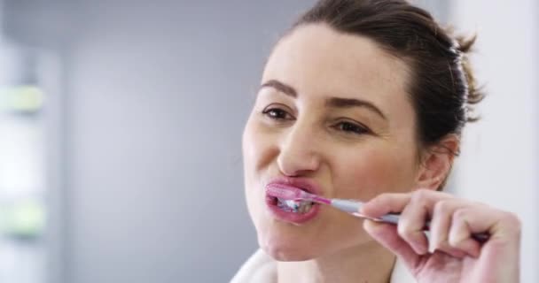 Γυναίκα, πρόσωπο και βούρτσισμα δοντιών με οδοντόβουρτσα, οδοντιατρική και στοματική υγιεινή με πρωινή ρουτίνα στο μπάνιο του σπιτιού. Γυναικείο καθαριστικό στόματος, φρέσκια αναπνοή και περιποίηση με οδοντόκρεμα και mockup space. - Πλάνα, βίντεο