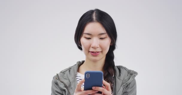 Telefon, mosoly és ázsiai nő gépel a stúdióban elszigetelt fehér háttér mockup helyet. Mobiltelefon, boldog és női személy a közösségi média, hálózatépítés vagy internetes tekercs, internetes böngészés és SMS. - Felvétel, videó