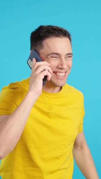 Video in de studio met blauwe achtergrond van een blije man aan het praten met de mobiele telefoon. Het frame begint leeg, de man verschijnt van onderen en verdwijnt dan aan de onderkant. - Video