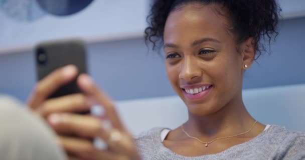 Telefon, SMS i szczęśliwa kobieta w łóżku z social media, wiadomości lub aplikacji komunikacyjnej w jej domu. Uśmiech, smartfon i afrykańska kobieta osoba w sypialni online do przeglądania, blog lub relaks podczas czytania. - Materiał filmowy, wideo