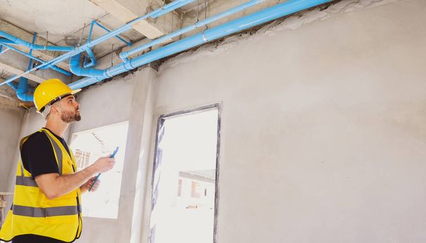 Nadzorca kaukaski mężczyzna hydraulik gospodarstwa klucz prace kontrolne naprawić niektóre niedokończone punkt DIY budynku rury kanalizacyjnej PVC rury kanalizacyjnej na piętrze łazienka domu podczas budowy mieszkaniowej. - Zdjęcie, obraz