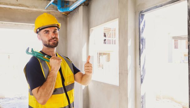 コーカサス州の男性プラム労働者はレンチツールを保持し,建設プロジェクト中に家でDIY建物の下水管とPVC配管パイプを成功裏に親指を示しています. - 写真・画像