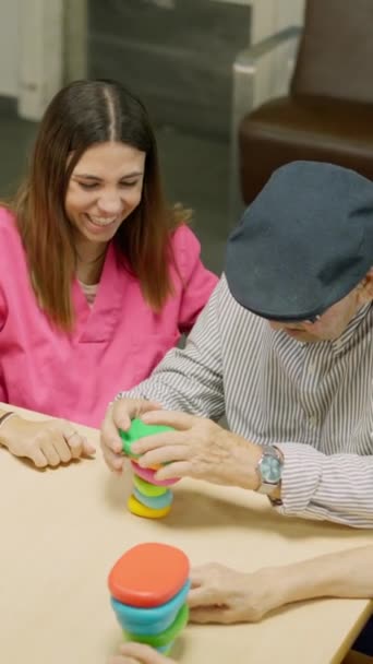 Vidéo d'un homme âgé résolvant un jeu de compétences compliqué dans un gériatrique et les gens le félicitent - Séquence, vidéo
