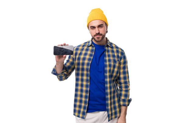 mladý stylový brunetka muž s brutální vousy a knír v čepici a košili drží smartphone mockup. - Fotografie, Obrázek