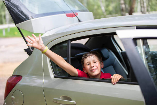 Un bambino allegro e gioioso in macchina mentre viaggia ondeggia la mano. - Foto, immagini