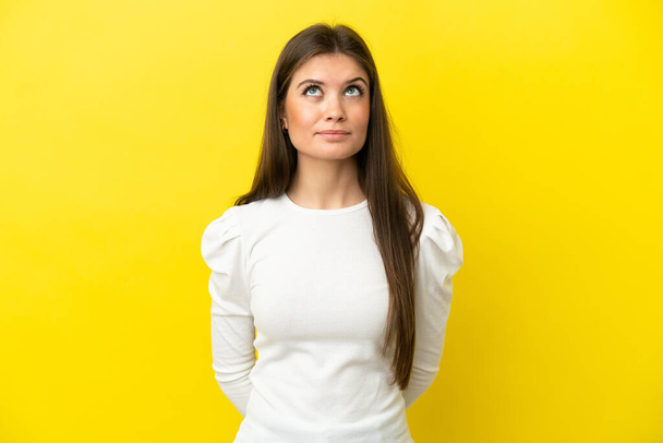 Young caucasian woman isolated on yellow background and looking up - Photo, Image