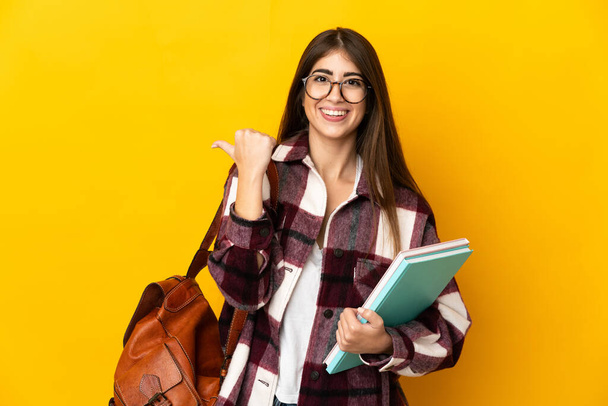 Jeune étudiante isolée sur fond jaune pointant vers le côté pour présenter un produit - Photo, image