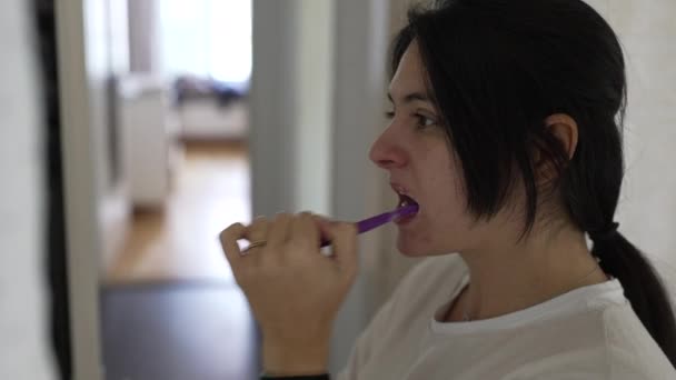 Kobieta myje zęby podczas porannego rytuału w łazience. Profil osoby patrzącej w lustro dbającej o higienę psychiczną - Materiał filmowy, wideo