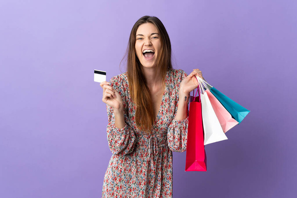 紫の背景に孤立した若いアイルランドの女性ショッピングバッグとクレジットカードを保持 - 写真・画像