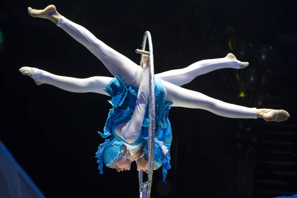 Две девушки-акробатки показывают номер цирка на темном фоне. Акробатическая производительность. - Фото, изображение