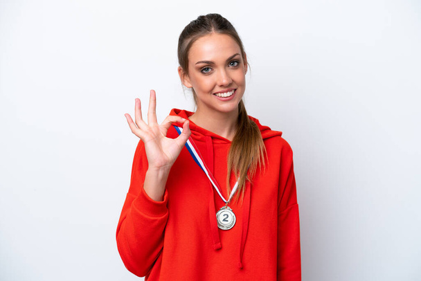 Young caucasian woman with medals isolated on white background showing ok sign with fingers - Foto, Imagen