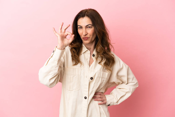 Mulher caucasiana de meia idade isolada em fundo rosa mostrando sinal ok com os dedos - Foto, Imagem