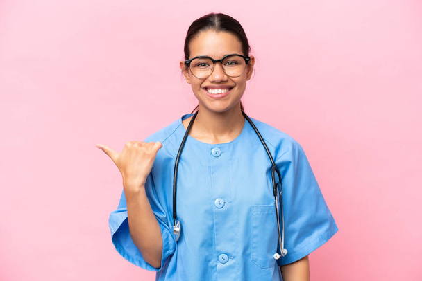 Mladá zdravotní sestra kolumbijská žena izolované na růžovém pozadí ukazuje do strany prezentovat produkt - Fotografie, Obrázek