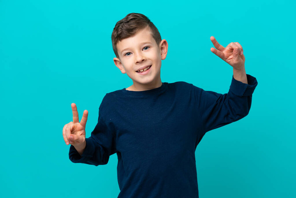 Malý chlapec izolované na modrém pozadí ukazující vítězství znamení s oběma rukama - Fotografie, Obrázek