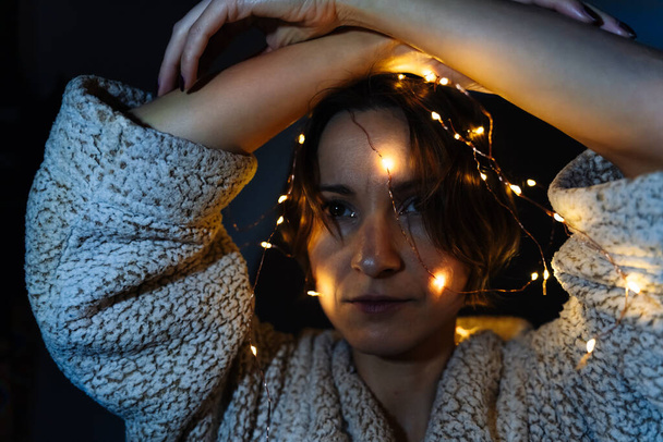 Une femme est décorée avec une guirlande de Noël rayonnante tenant ses mains au-dessus de sa tête. - Photo, image