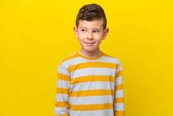 Маленький білий хлопчик ізольований на жовтому тлі робить сумніви жестом, дивлячись збоку - Фото, зображення