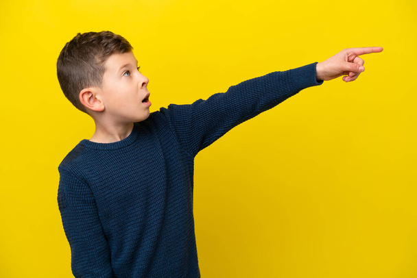 Pieni valkoihoinen poika eristetty keltaisella taustalla osoittaa poispäin - Valokuva, kuva