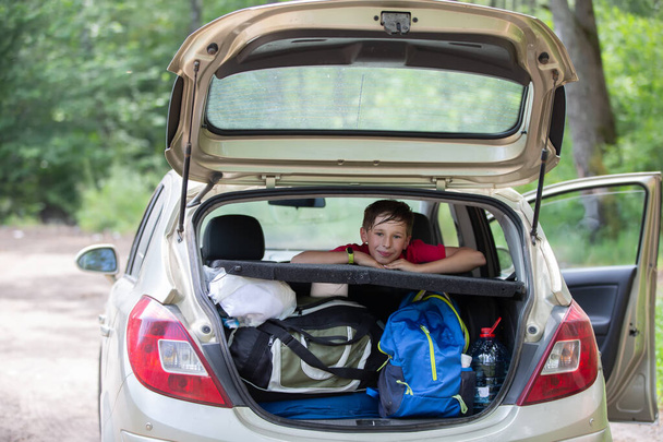 Uma criança numa viagem. Um rapaz olha para fora da bagageira de um carro cheio de sacos enormes. - Foto, Imagem