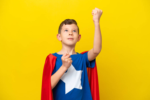 Kleiner kaukasischer Junge isoliert auf gelbem Hintergrund im Superheldenkostüm und feiert einen Sieg - Foto, Bild