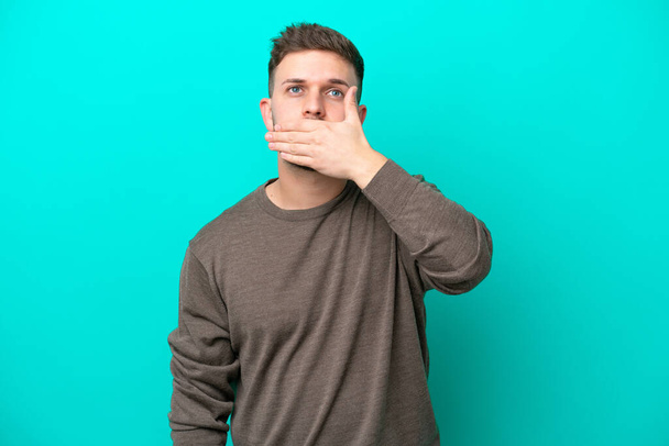 Jonge blanke man geïsoleerd op blauwe achtergrond bedekken mond met de hand - Foto, afbeelding