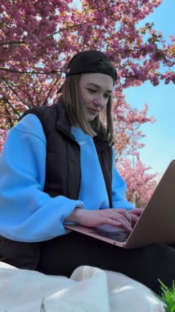жінка зовні працює над ноутбуком, квітучим сакурою на фоні позаштатної концепції - Кадри, відео