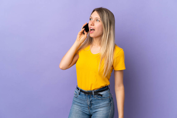Young blonde woman isolated on purple background keeping a conversation with the mobile phone - Photo, Image