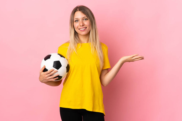 Jeune joueur de football femme isolée sur fond rose tenant copyspace imaginaire sur la paume - Photo, image