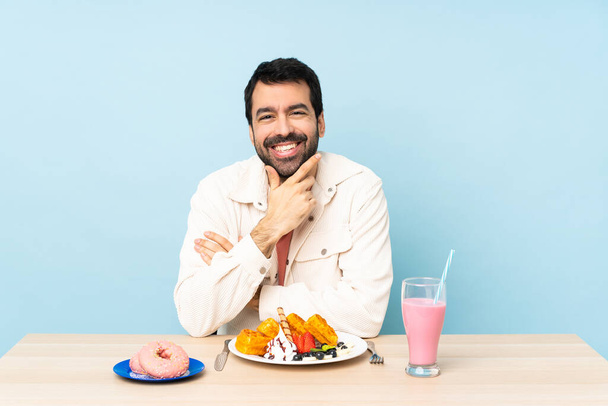 Άνθρωπος σε ένα τραπέζι που τρώει βάφλες και ένα μιλκσέικ χαμογελαστό - Φωτογραφία, εικόνα